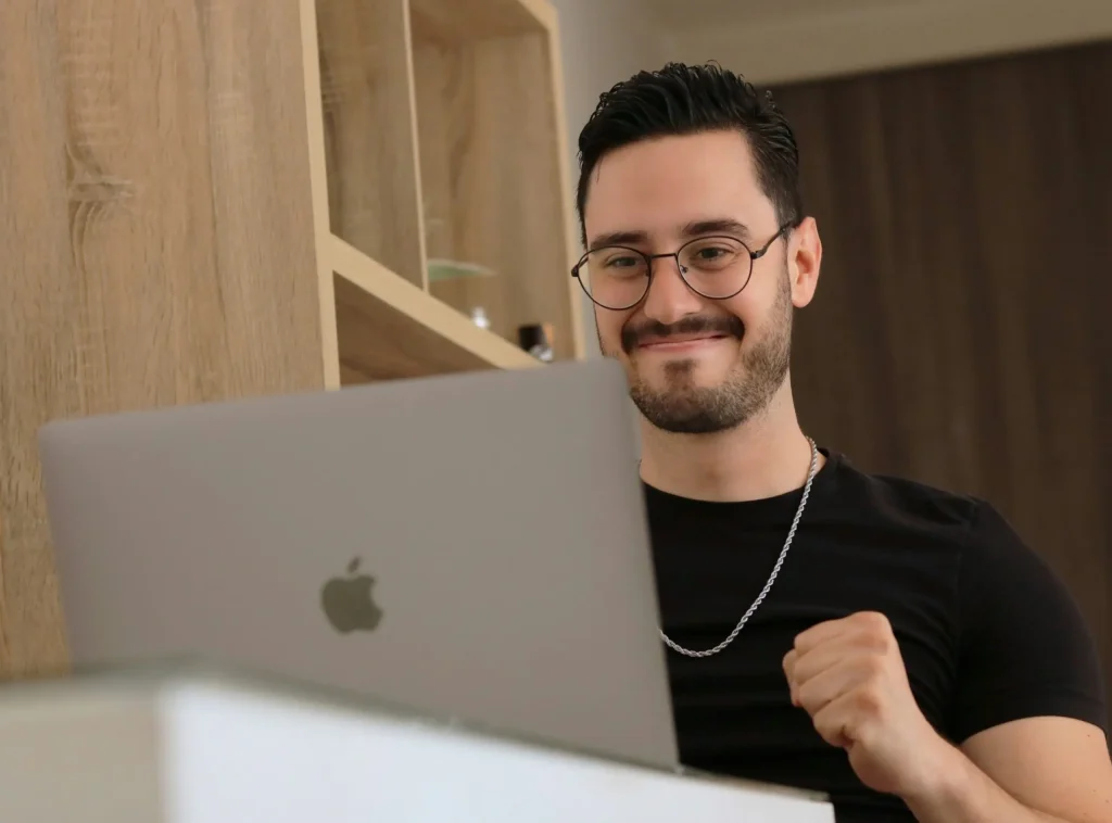 Smiling man making a small fist pump while looking at laptop