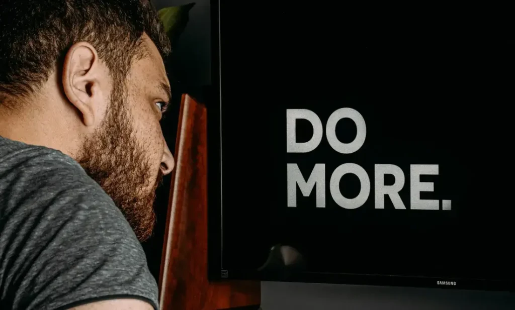 Bearded man looking at a screen that says "DO MORE" in bold letters