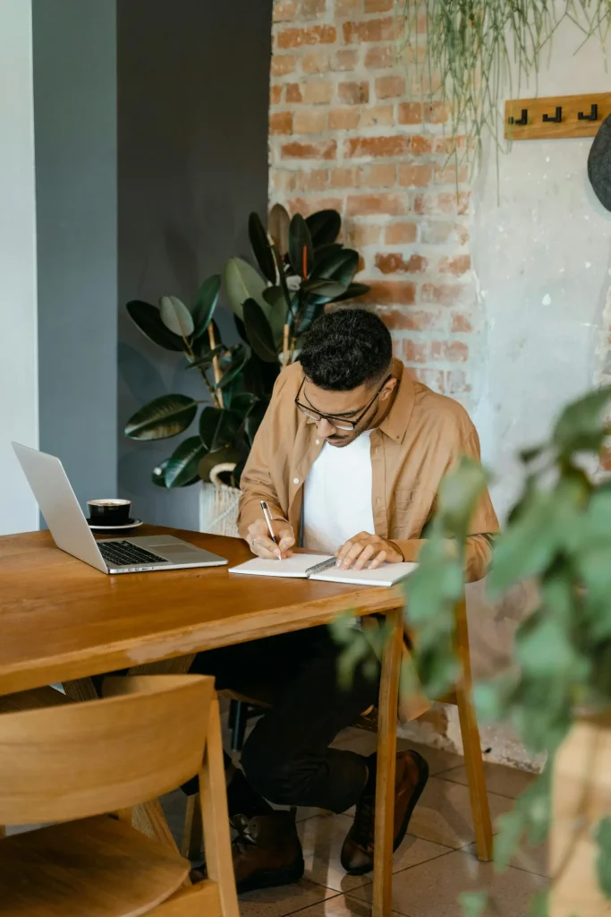 Structuring the path to lasting results Man sitting at a desk writing in a notebook beside a laptop