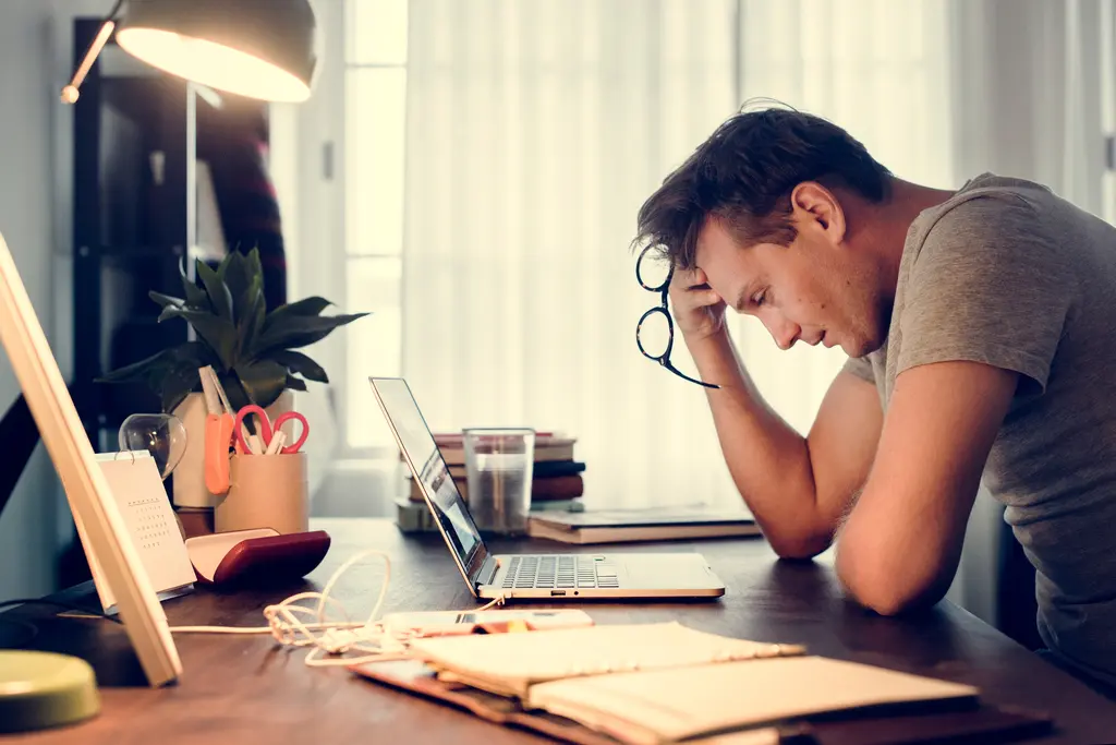 Overwhelmed professional struggling with focus and follow-through Frustrated man working at laptop with head in hand